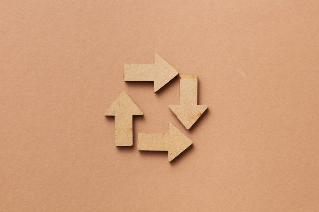 pexels-photo-7679935-7679935 Close-up of a recycling symbol made from wooden arrows on a beige background.